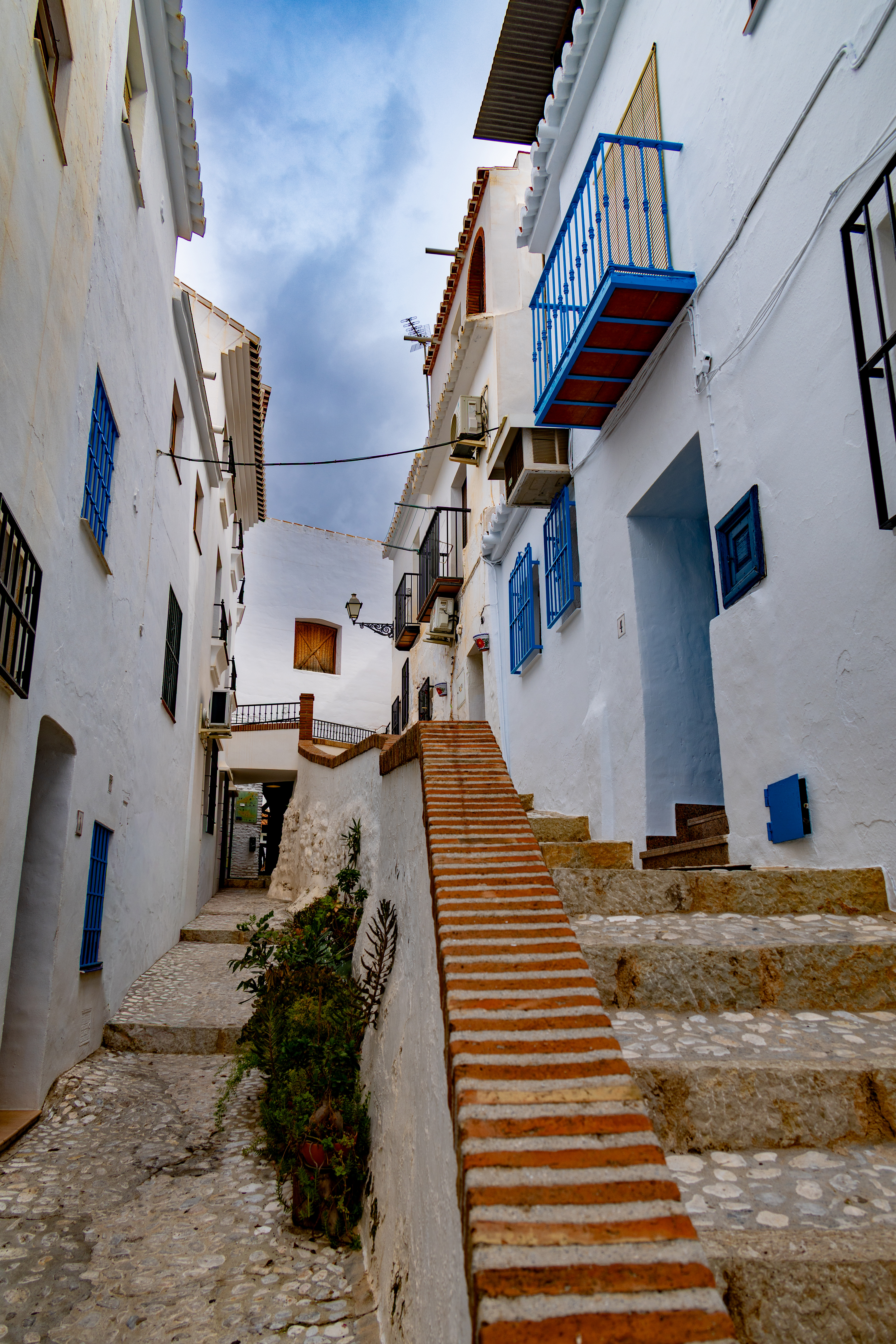 Enge Gasse mit weissen Häusern, blauen Balkonen und einer Backsteintreppe